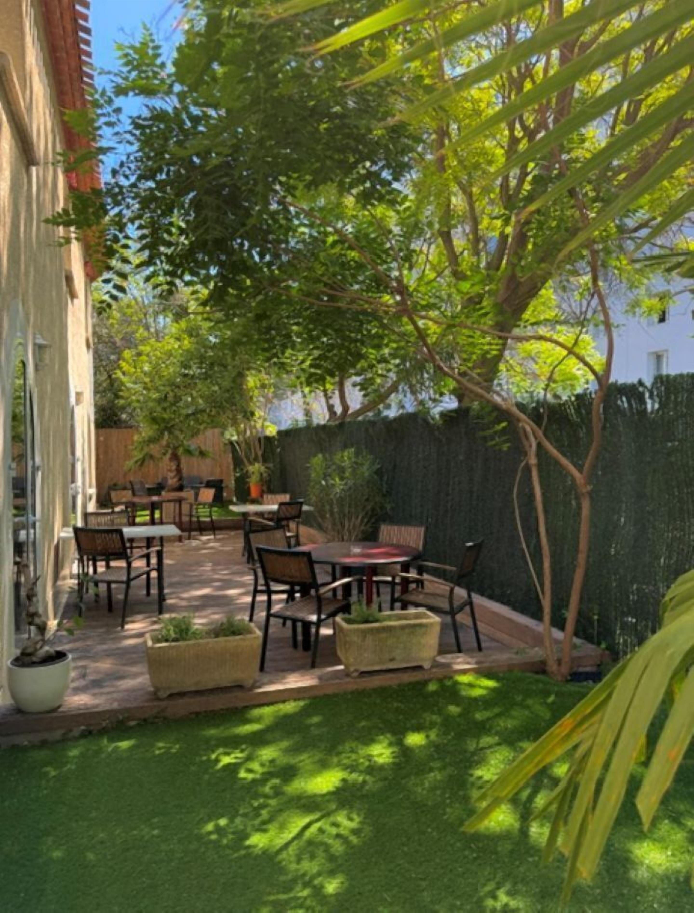 Een terras met tuinmeubilair, een kleine tuin en een gebouw op de achtergrond.