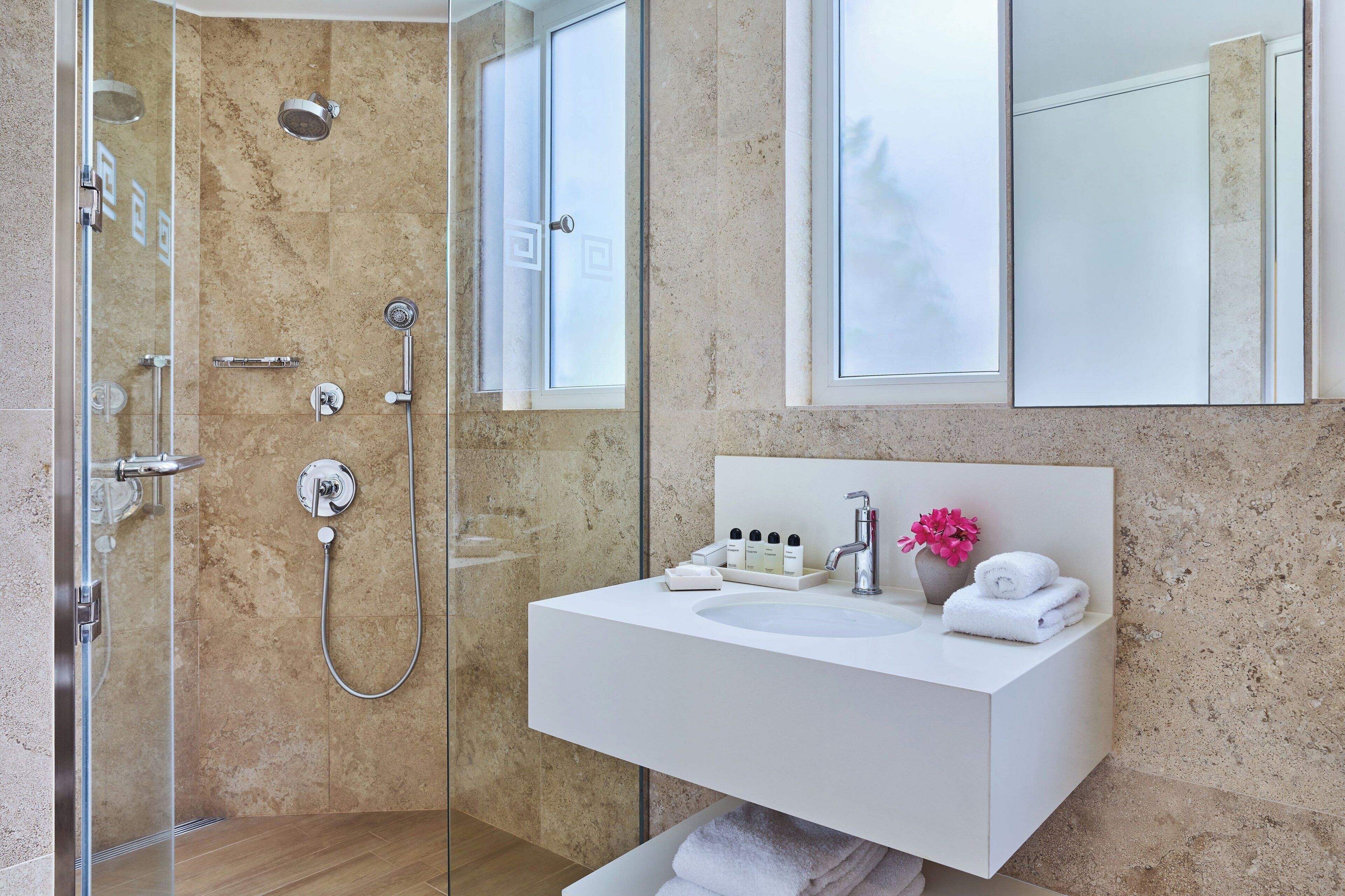 A modern bathroom with a glass-enclosed shower, a white sink with toiletries, and a large mirror.