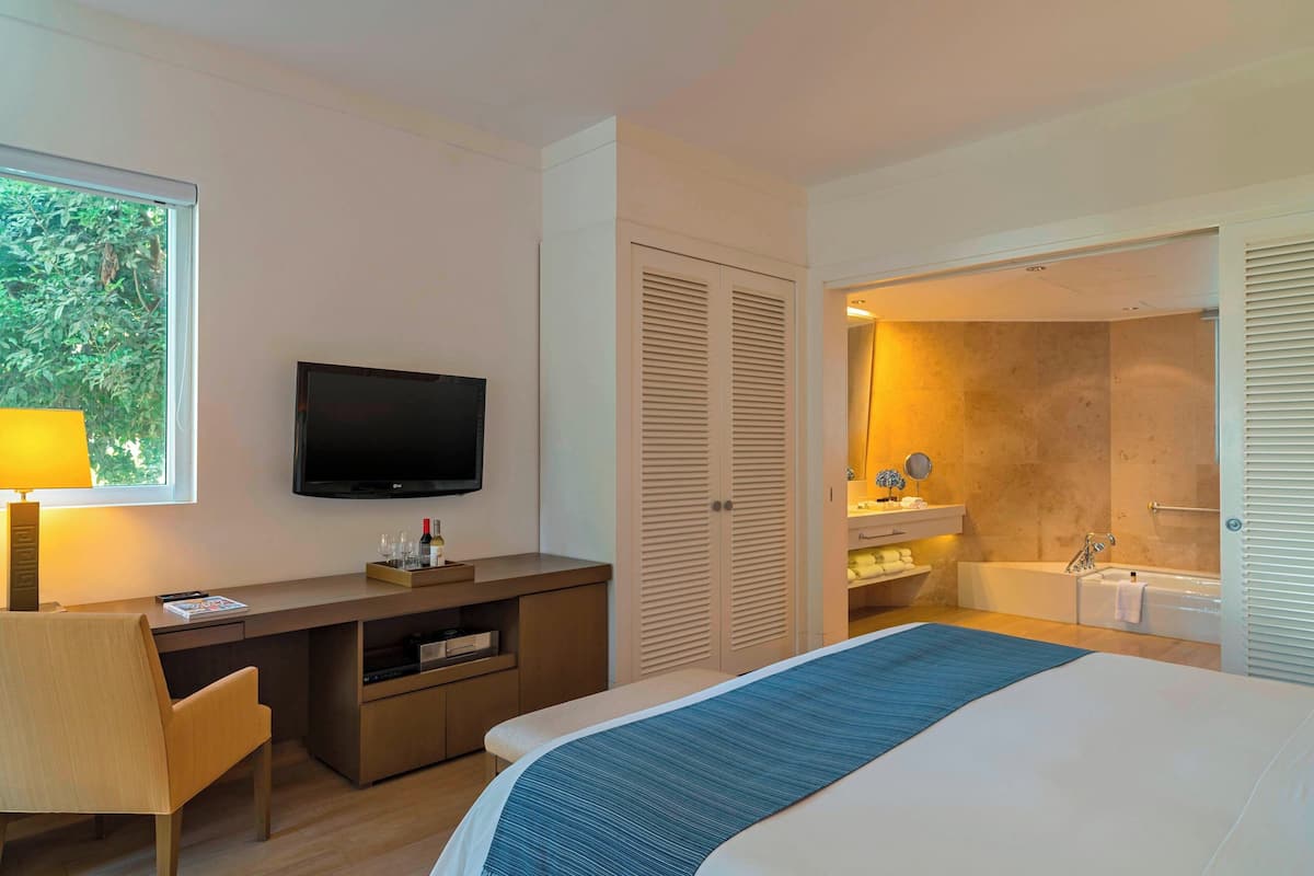 Une chambre d’hôtel moderne équipée d’un lit, d’un bureau, d’une télévision et d’une salle de bain avec baignoire et lavabo.