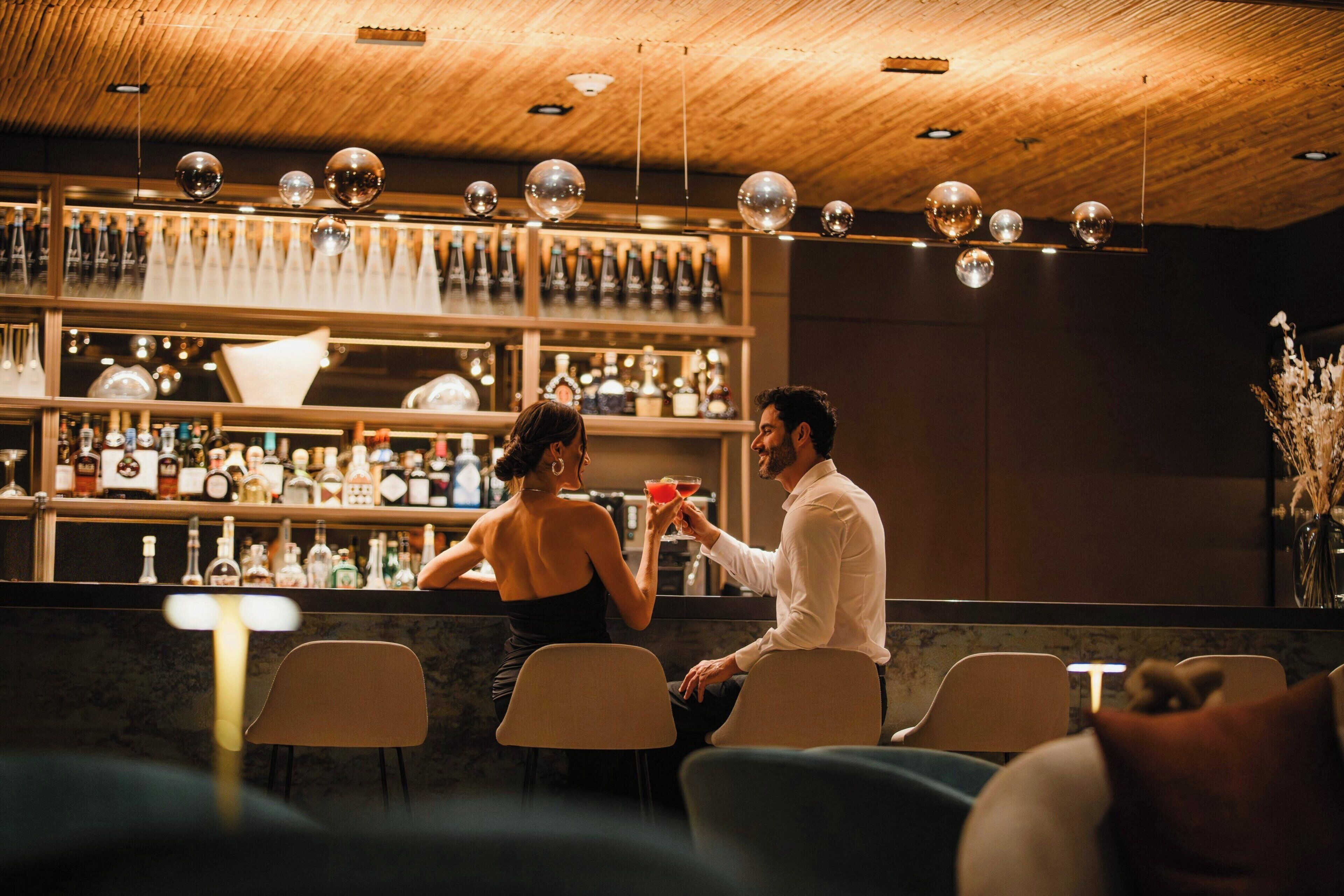 A bar area with a wooden ceiling, hanging spherical light fixtures, and shelves stocked with bottles.