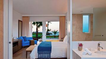Habitación de hotel con una cama, un sofá azul, una mesita, un baño con lavamanos y espejo, y vistas a un paisaje verde.