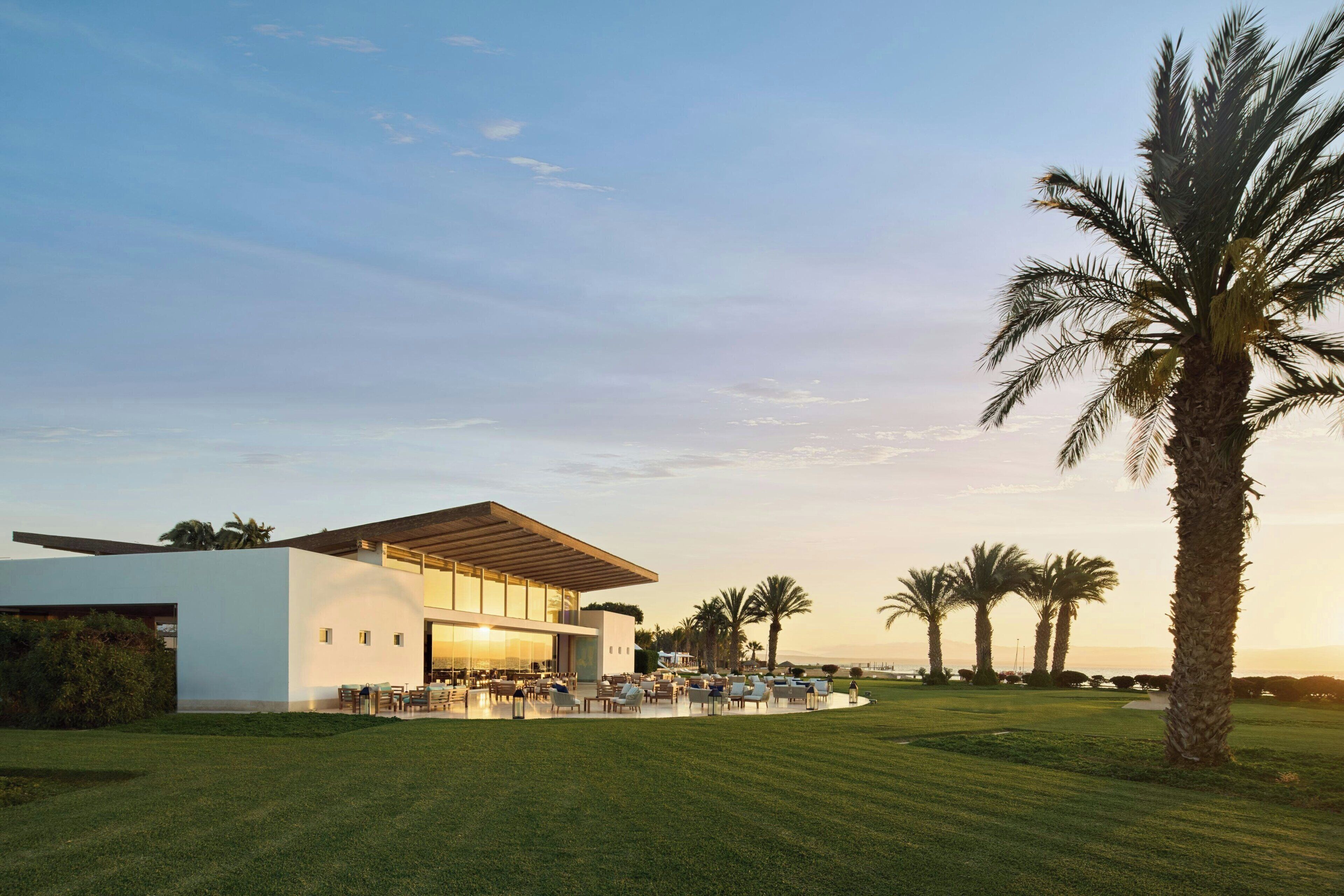A modern building with a flat roof and large windows, surrounded by a well-maintained lawn and palm trees.