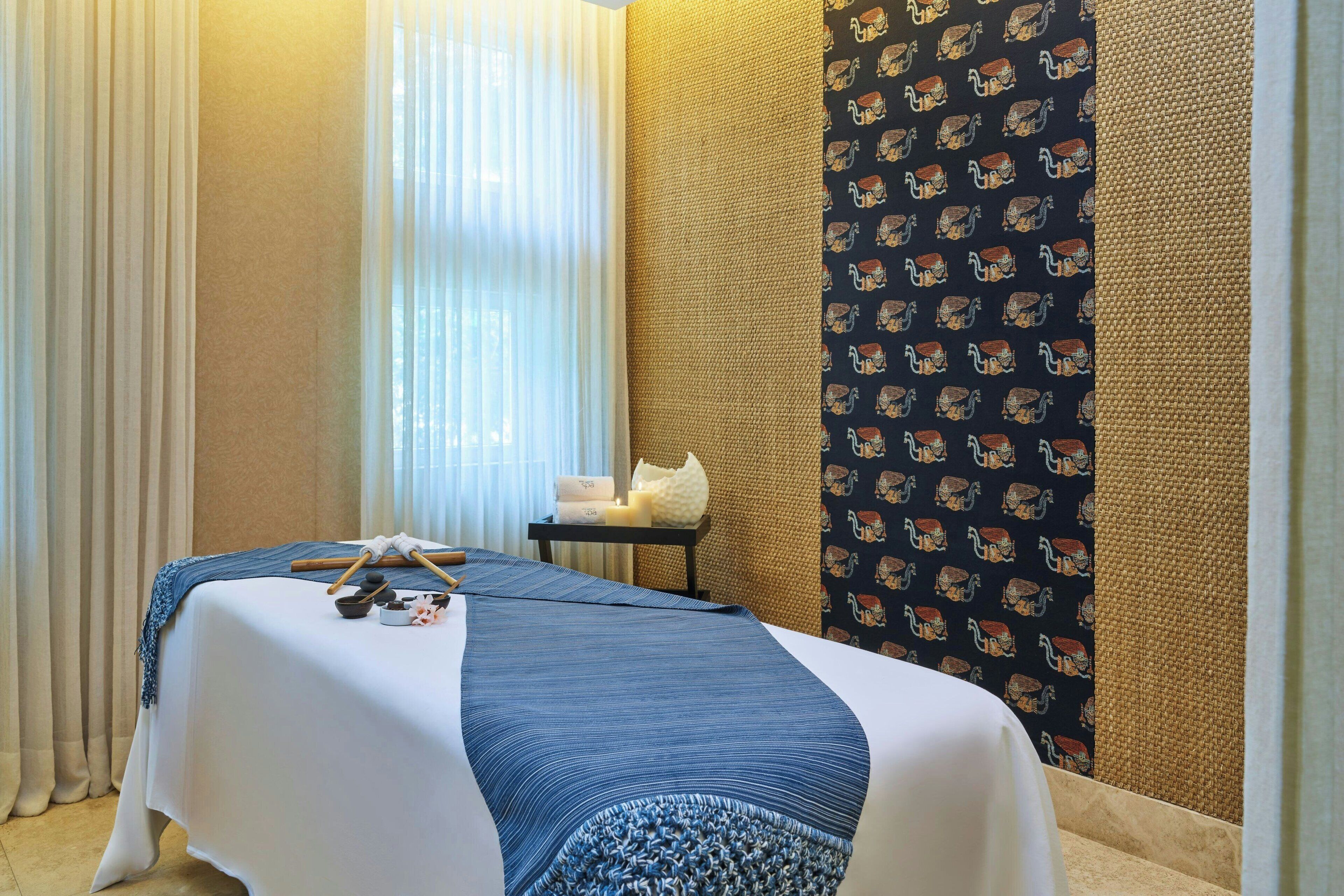 A hotel room with a bed, a small table with towels, and a patterned wall.