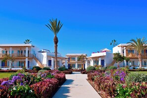 A modern hotel with a central pathway, surrounded by lush gardens and palm trees.