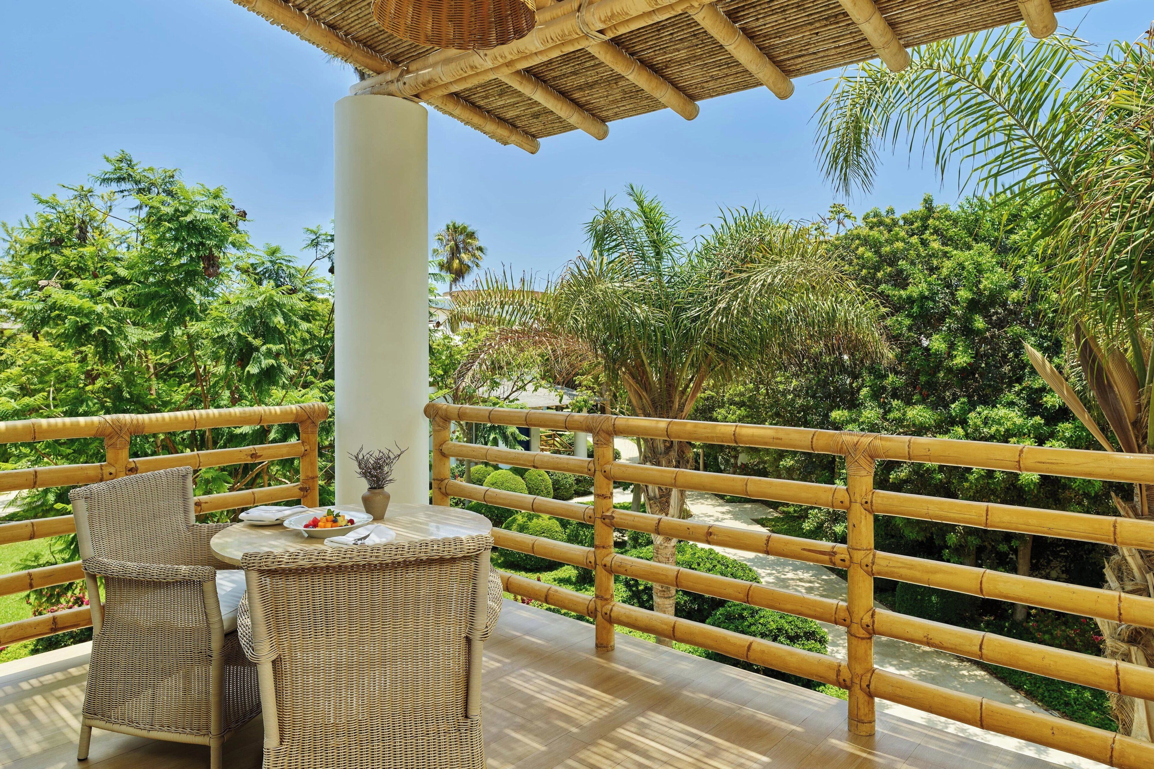 A balcony with wicker furniture, a bamboo railing, and a view of lush greenery.