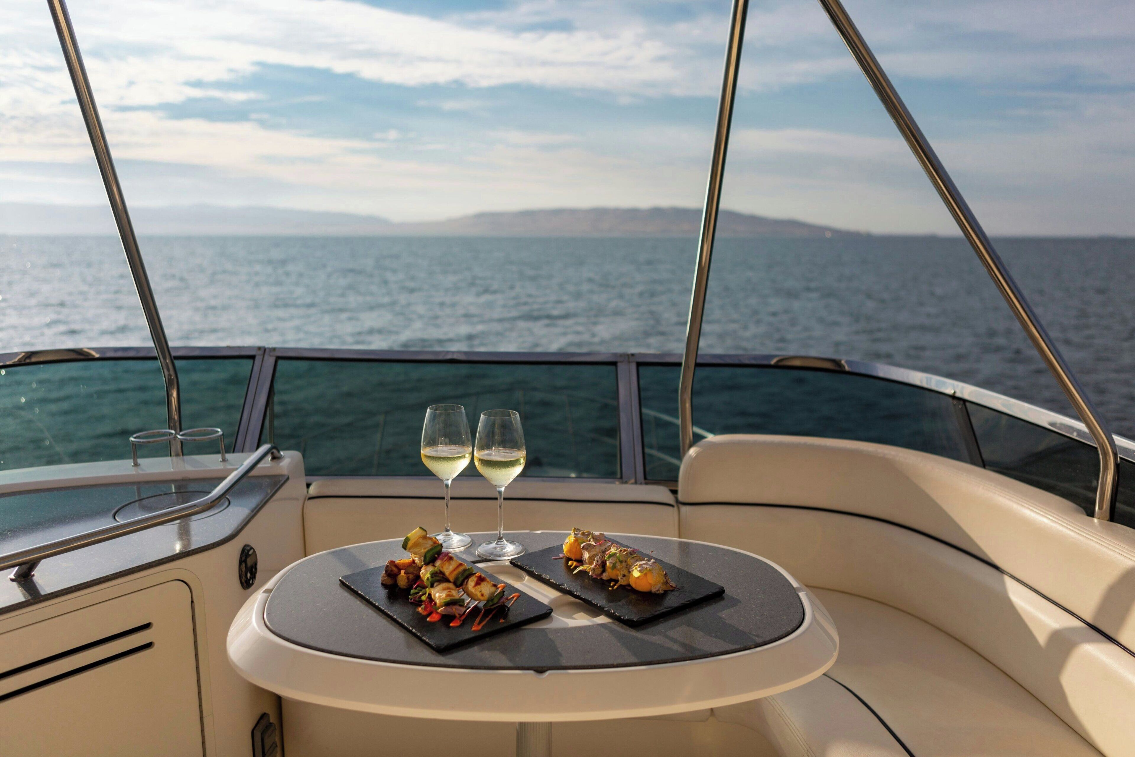 Une table avec deux assiettes de nourriture et deux verres de vin sur le pont d’un bateau, avec vue sur la mer.