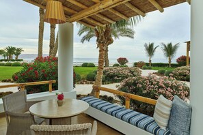 A covered outdoor seating area with a table and chairs, overlooking a landscaped garden with palm trees and flowering plants.