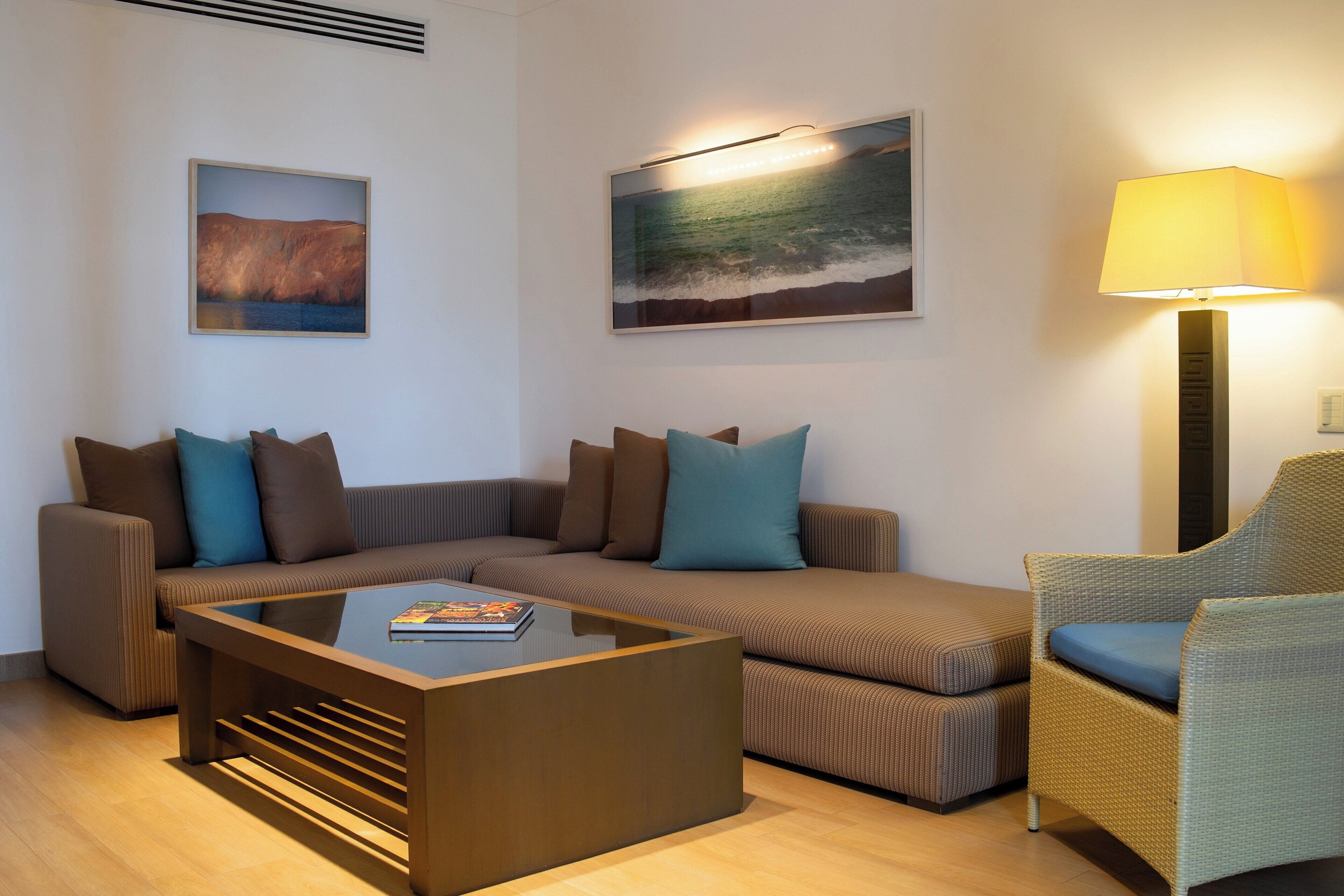 Una sala de estar moderna con un sofá seccional, una mesa de centro de vidrio, un sillón de mimbre y dos cuadros colgados en la pared.