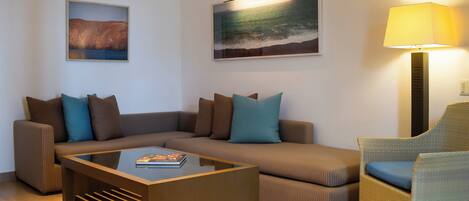 Una sala de estar moderna con un sofá seccional, una mesa de centro de vidrio, un sillón de mimbre y dos cuadros colgados en la pared.