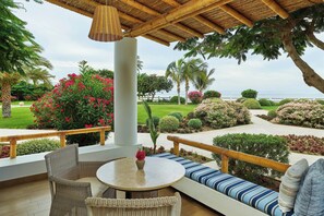 An outdoor seating area with wicker furniture, a round table, and a view of the sea.