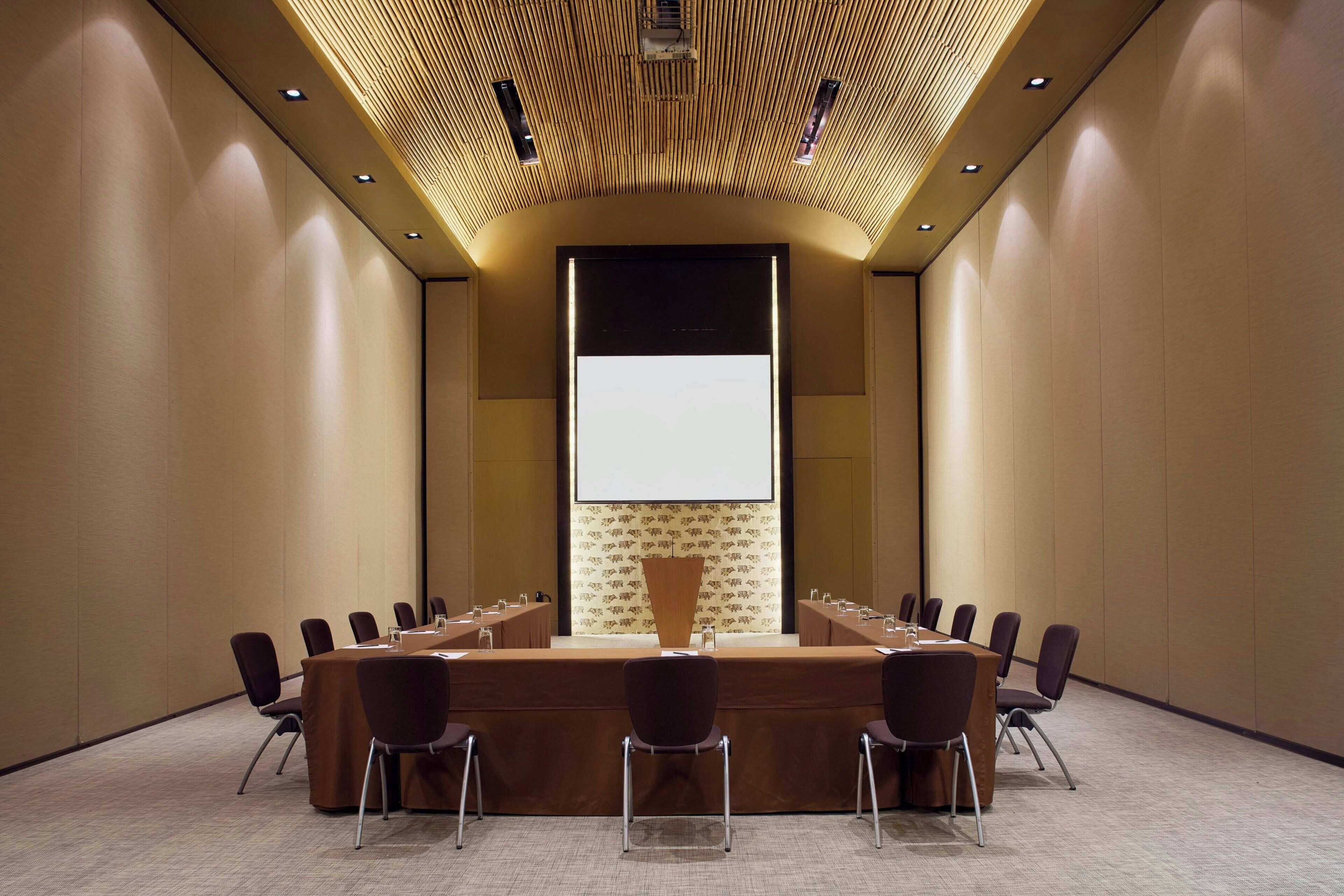 Un salón de conferencias con una larga mesa, sillas, una pantalla de proyector y un papel tapiz decorado.