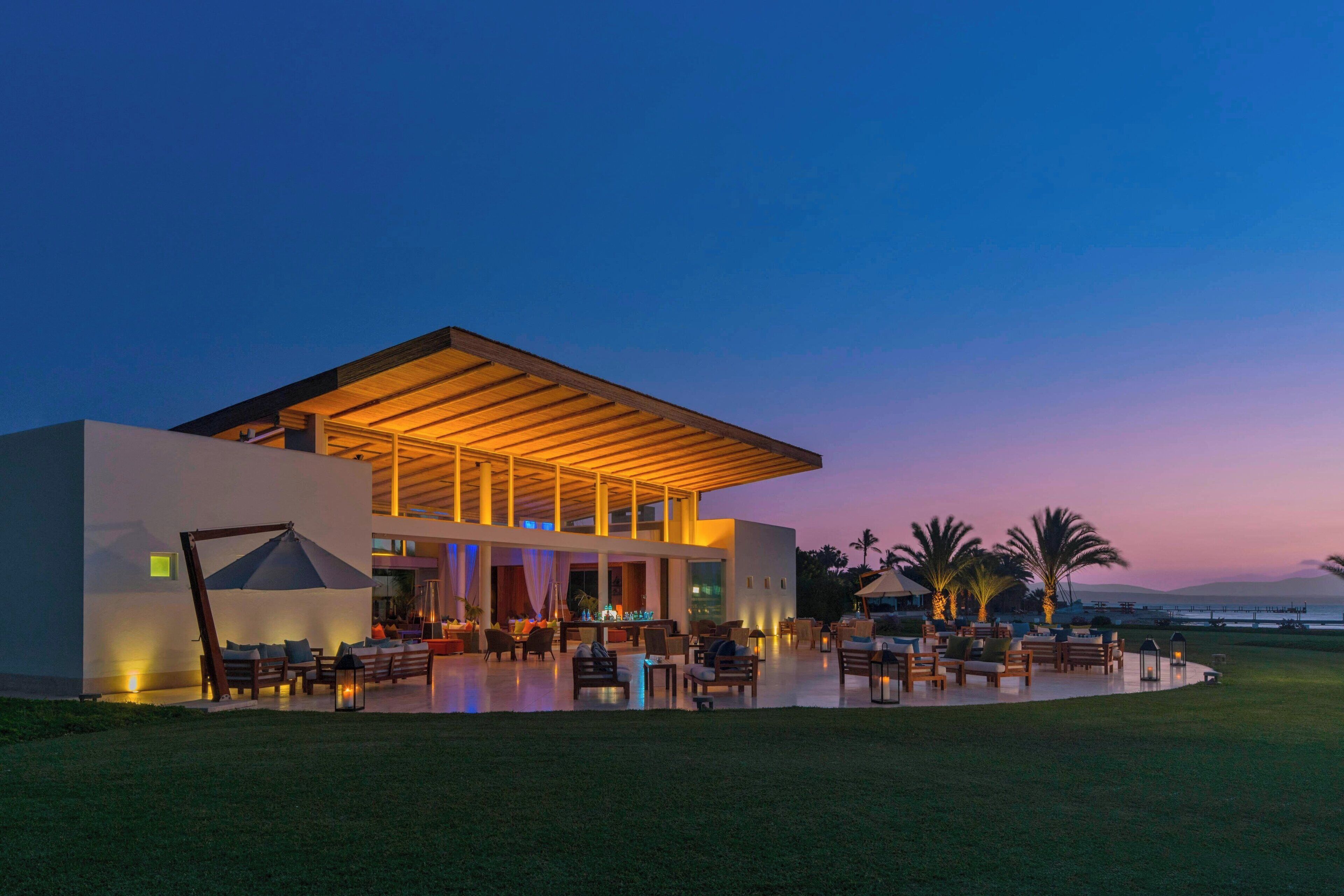 A modern building with a covered outdoor seating area, a pool, and a view of the ocean.
