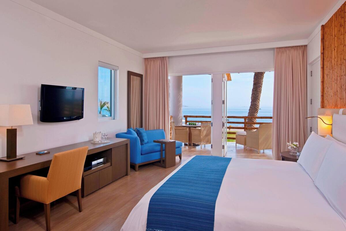 Une chambre d’hôtel comprenant un lit, un bureau, une télévision, un canapé et un balcon avec vue sur la mer.