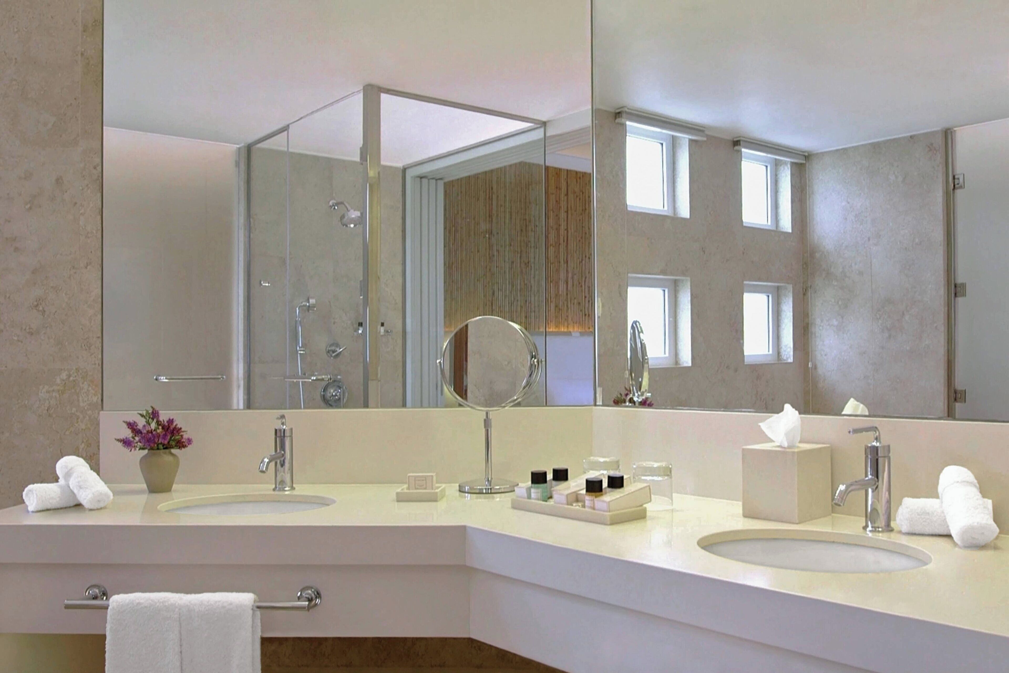 A modern bathroom with two sinks, a large mirror, and a shower area.