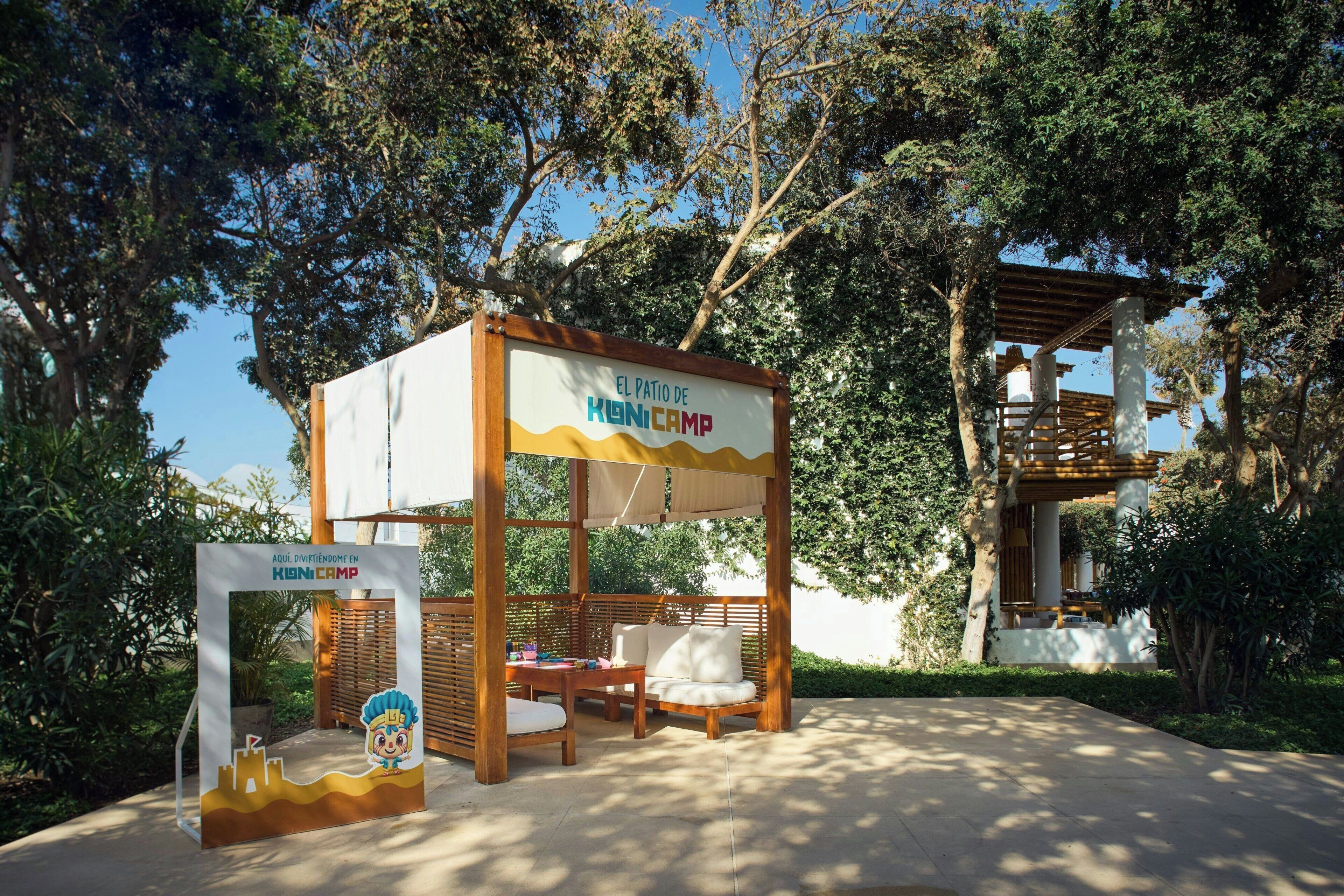 Un pabellón de madera con un letrero que dice 'El Patio de KONICAMP' y un área de estar con una mesa y sillas.