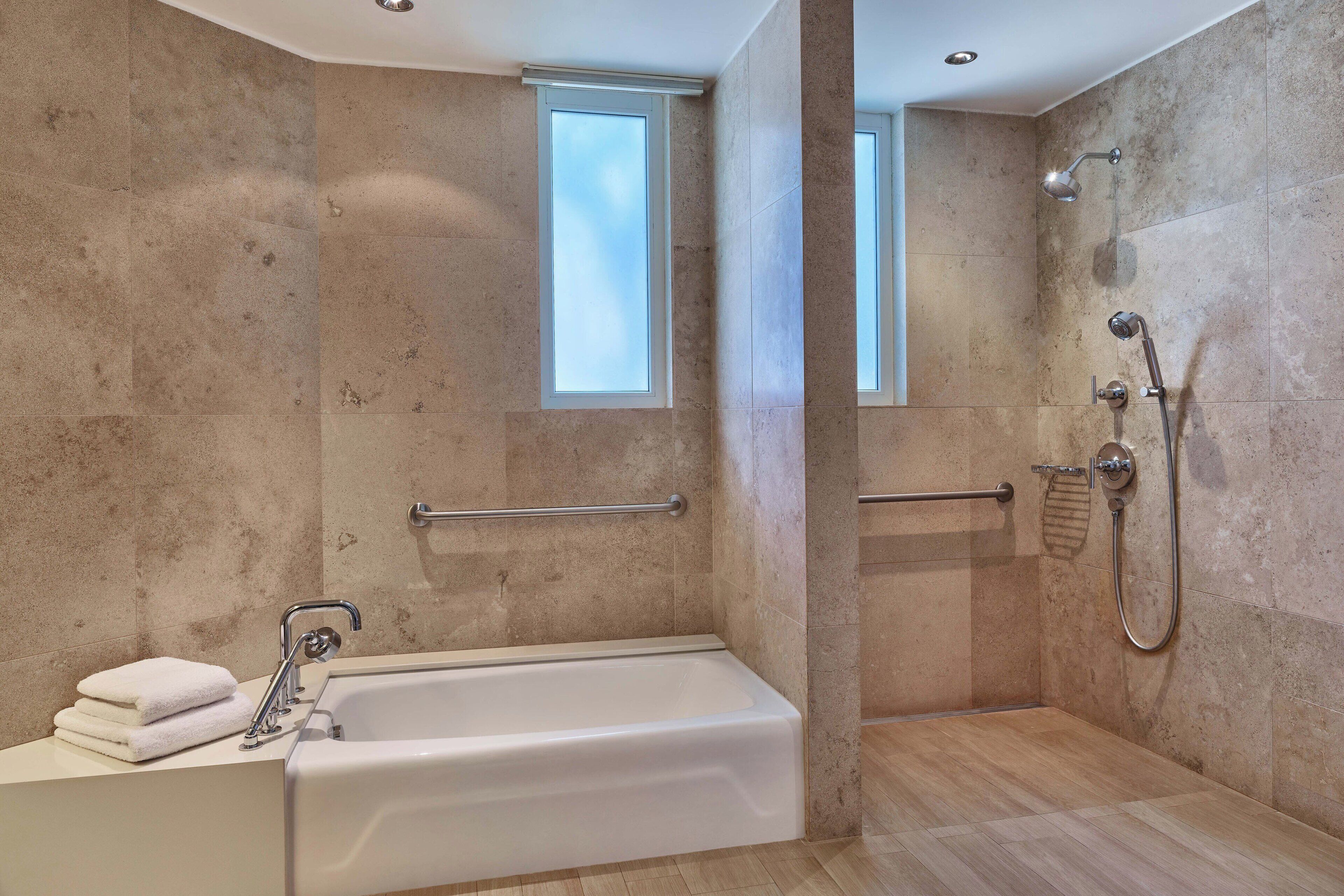 A modern bathroom with a bathtub, shower, and handrails.