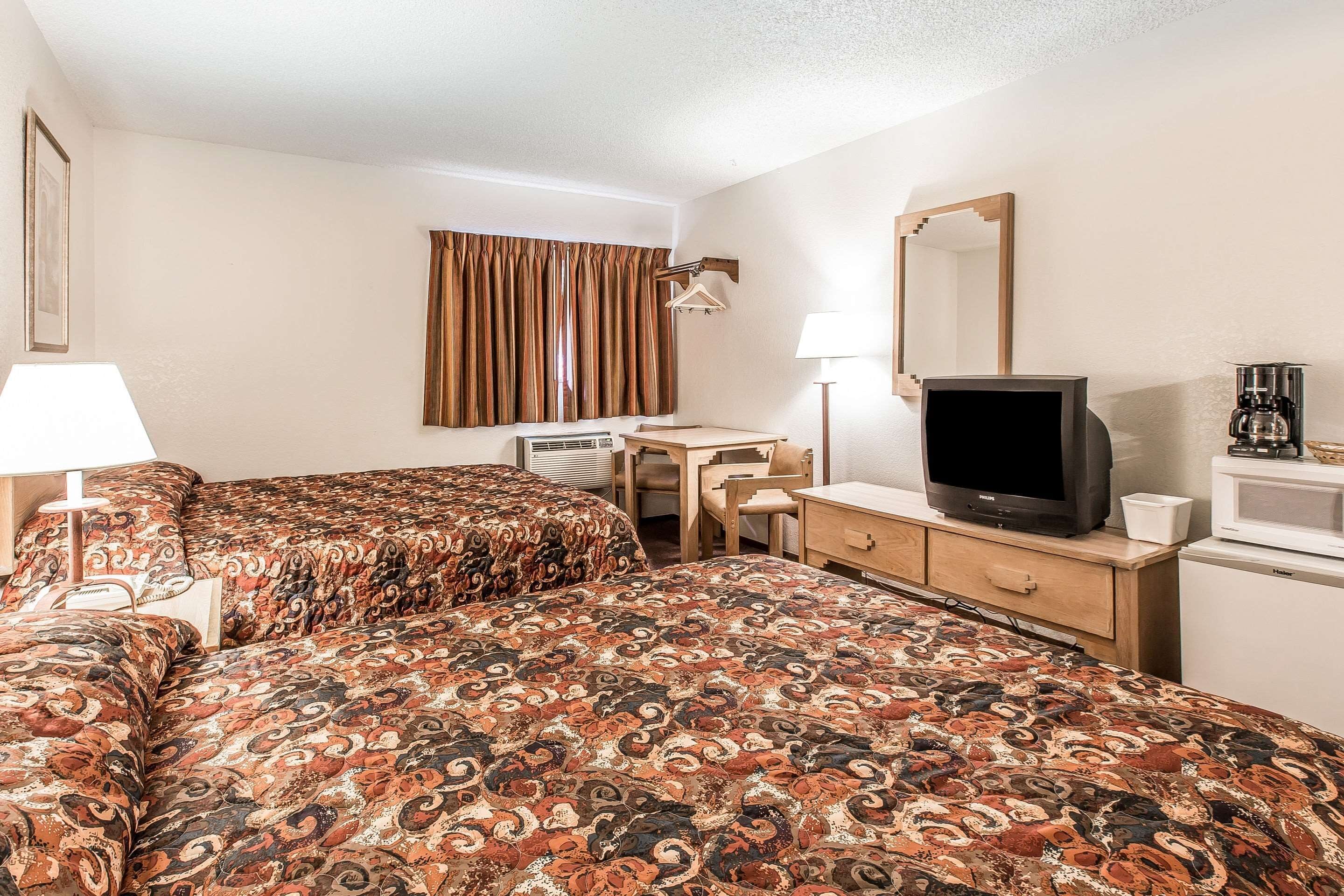 A hotel room with two beds, a desk, a television, a mirror, and a coffee maker.