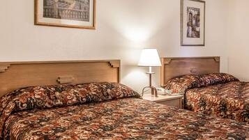 Quarto de hotel com duas camas, uma mesinha de cabeceira, uma luminária e quadros nas paredes.
