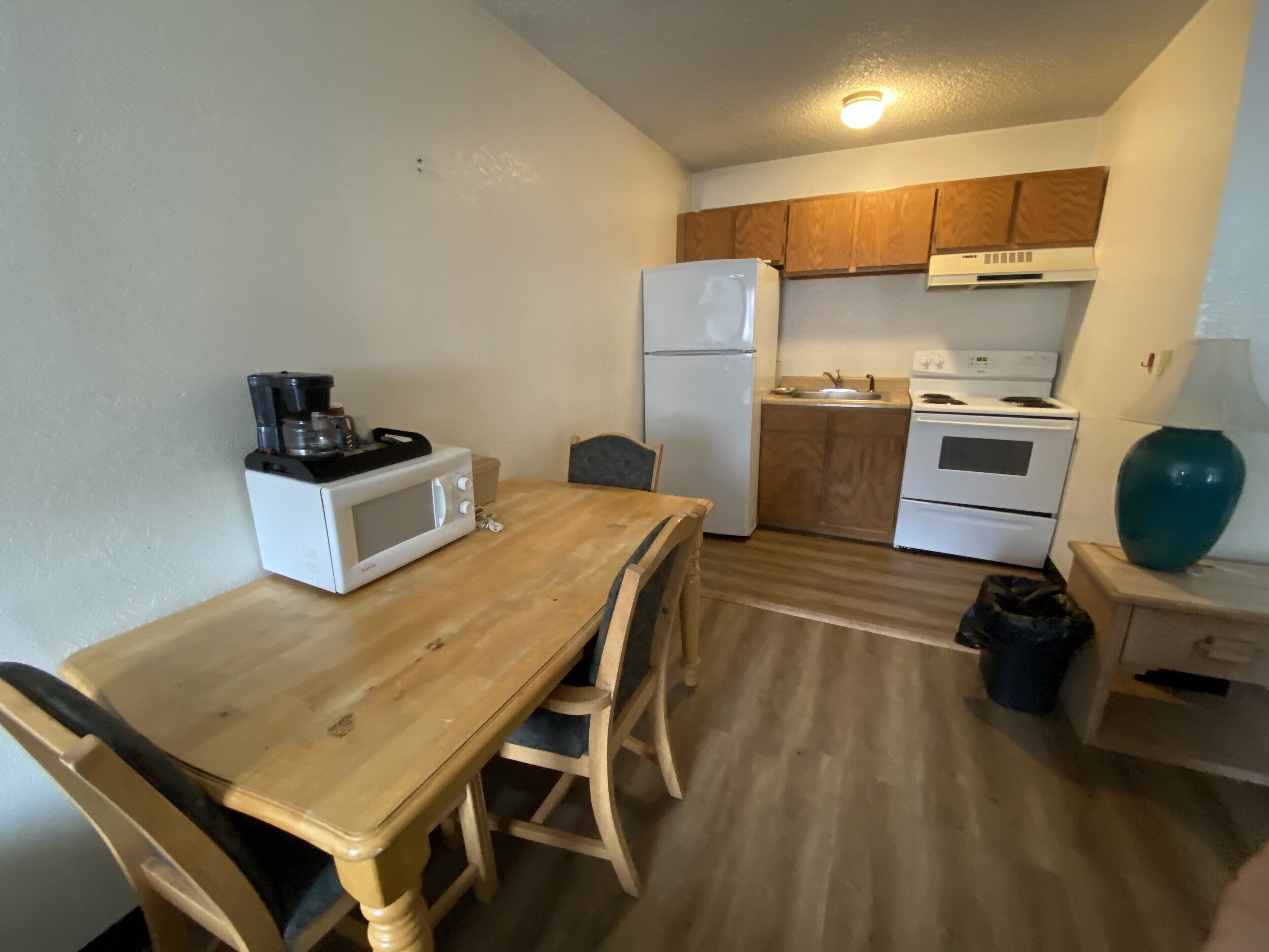 A compact kitchen with a wooden table, chairs, a microwave, a refrigerator, a stove, and a sink.