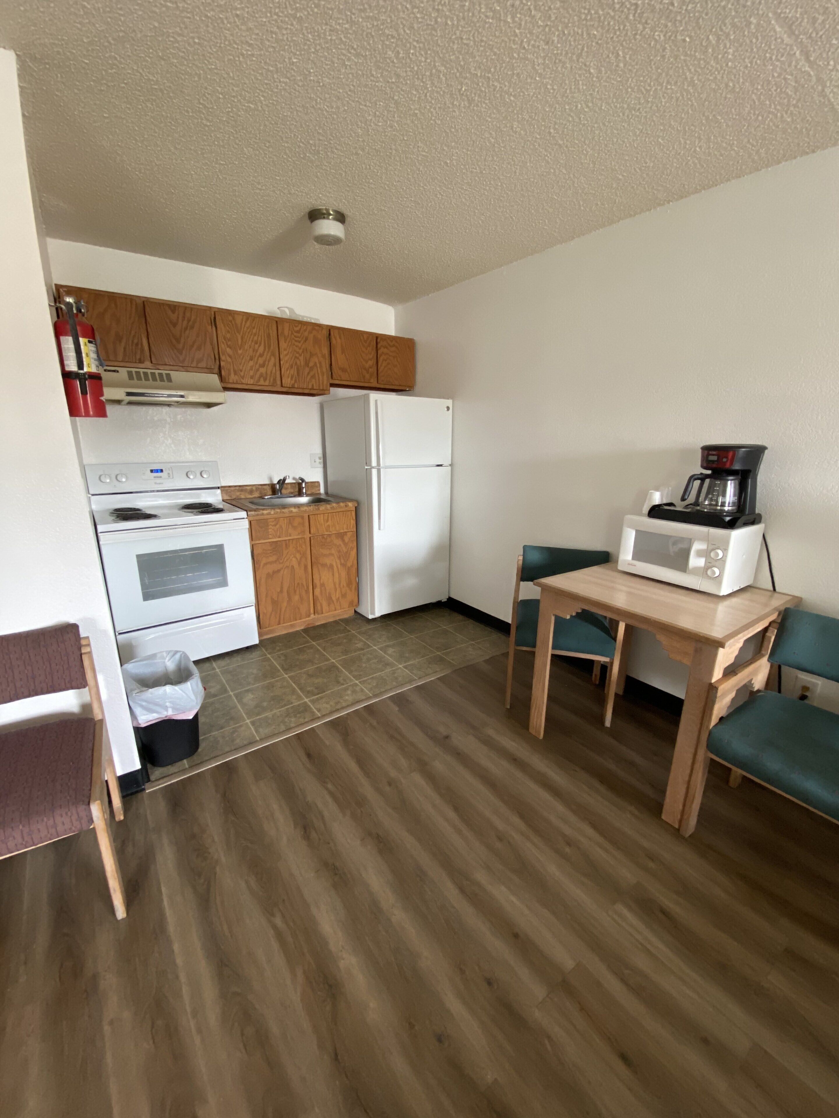 A compact kitchen with wooden cabinets, a white stove, a white refrigerator, and a microwave on a wooden table.