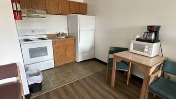 A compact kitchen with wooden cabinets, a white stove, a white refrigerator, and a microwave on a wooden table.