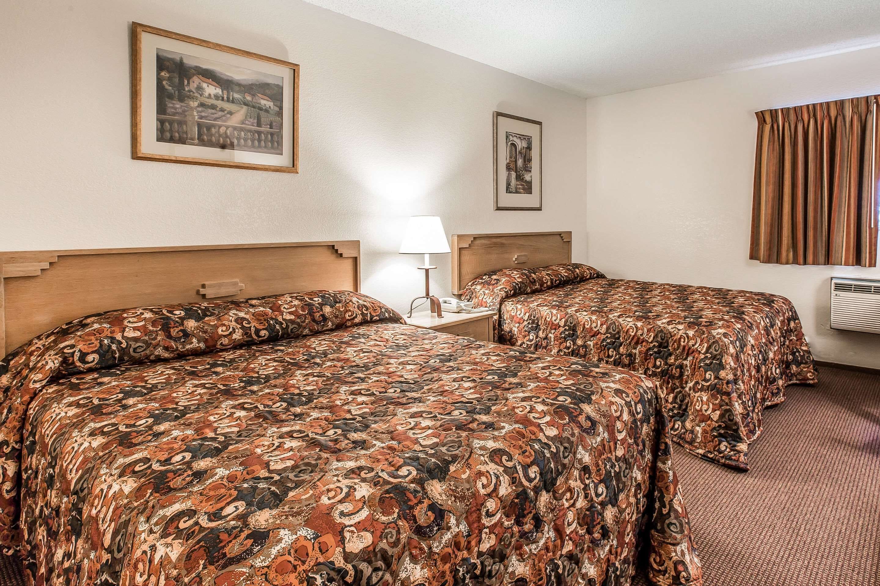 A hotel room with two beds, a nightstand, a lamp, and framed pictures on the wall.