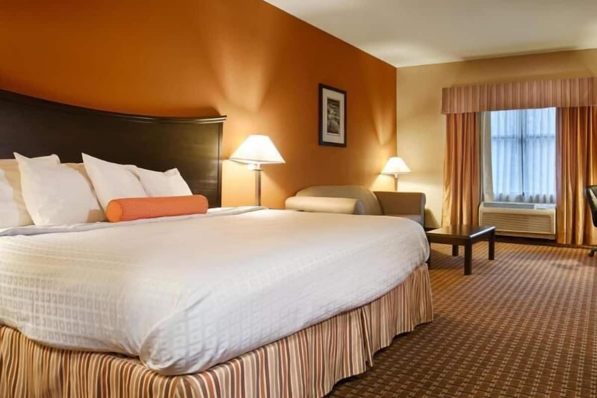 A hotel room with a large bed, two bedside tables, a chair, a window with curtains, and a wall-mounted picture.