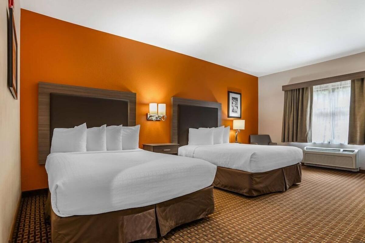 A hotel room with two beds, a large mirror, wall-mounted lamps, a flat-screen TV, and an air conditioning unit.