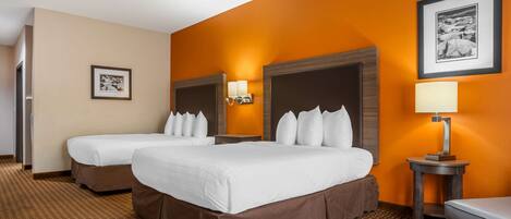A hotel room with two beds, a brown carpet, a wall with an orange accent, and a framed picture on the wall.