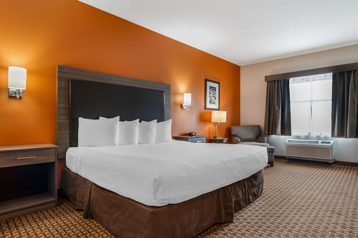 A hotel room with a large bed, a desk, a chair, a lamp, and a window with curtains.