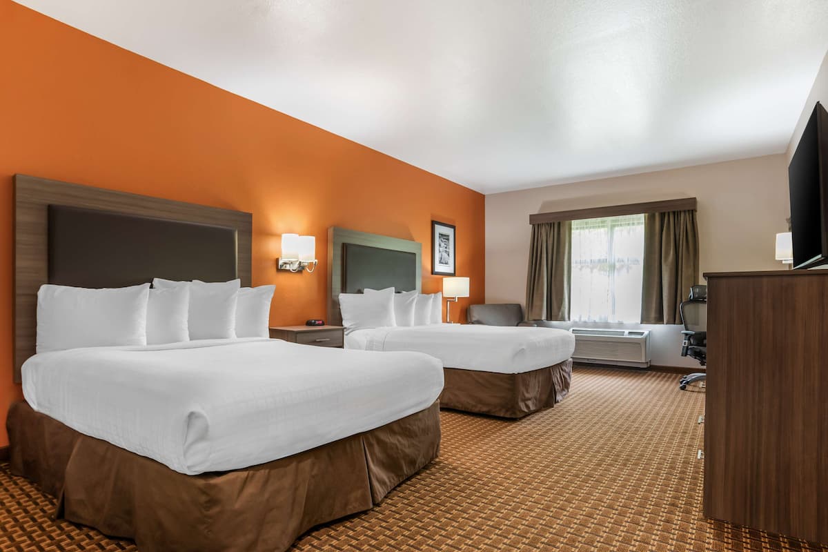 A hotel room with two beds, a desk, a chair, a TV, and a window with curtains.