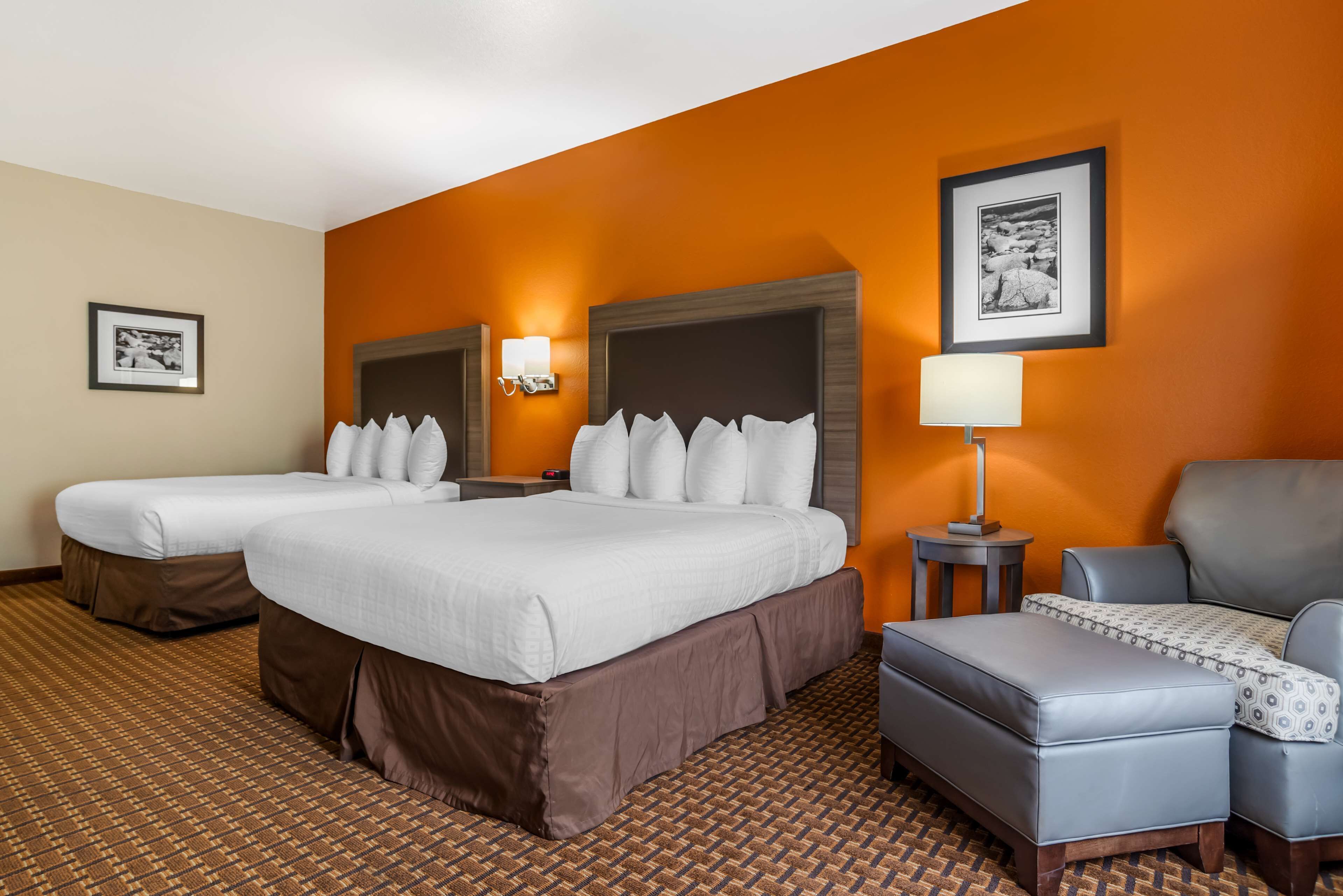 A hotel room with two beds, a sofa, a chair, and a small table with a lamp.