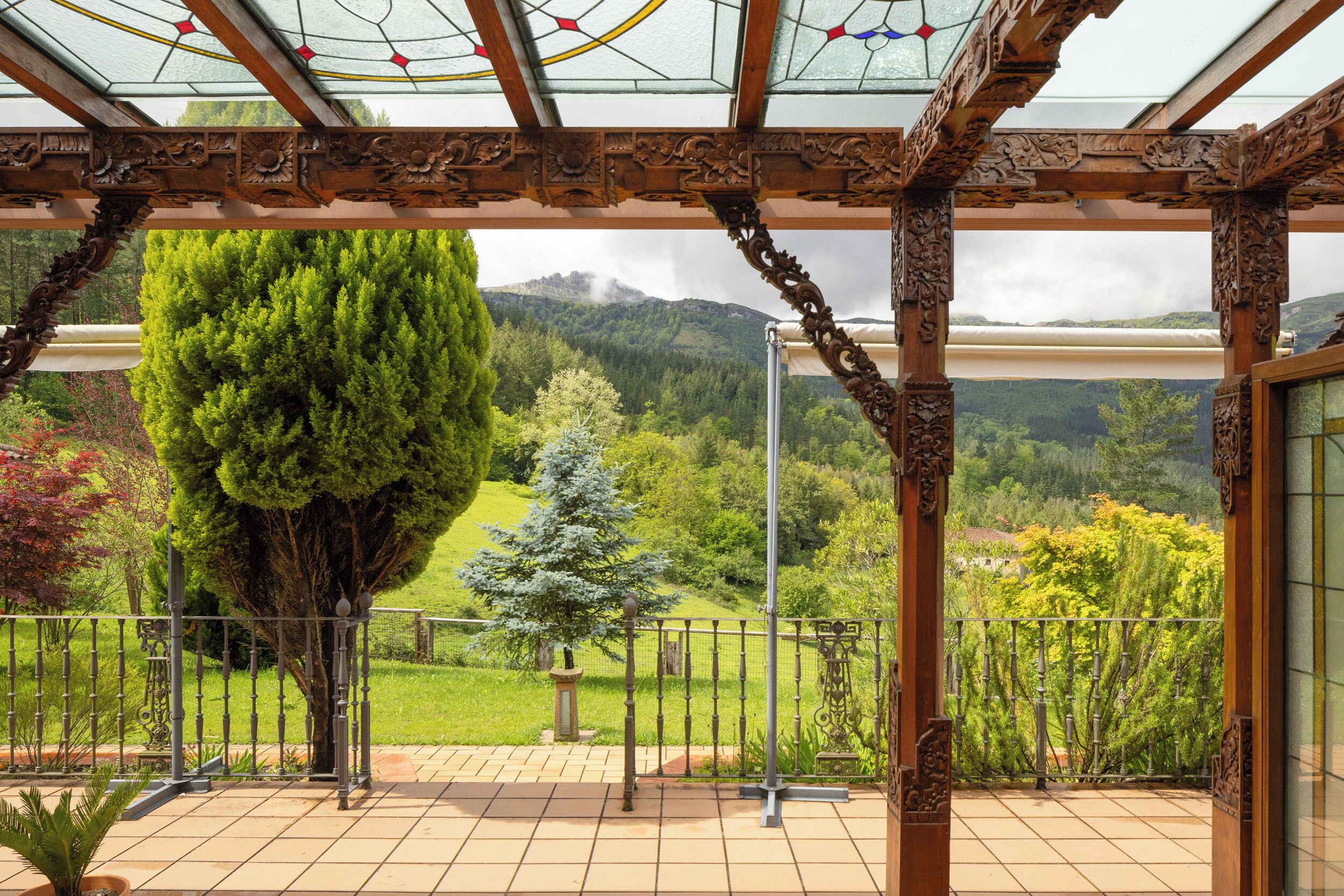 Un espace extérieur abrité, offrant une vue sur un paysage montagneux, un grand arbre et doté d’un sol carrelé.