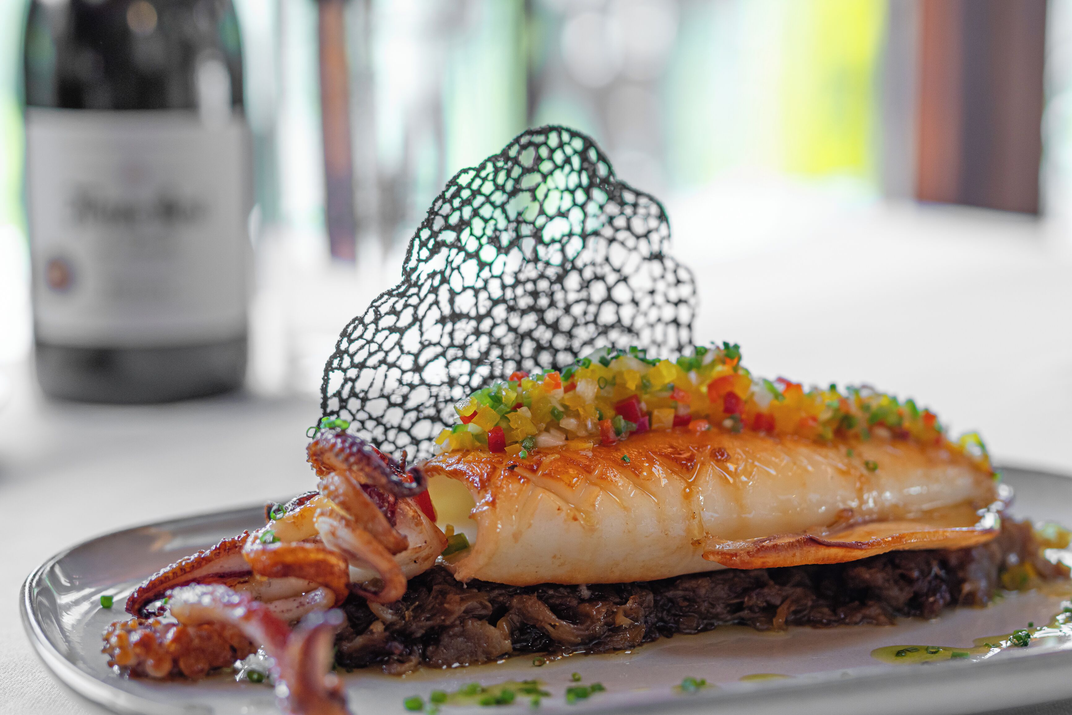 A seafood dish with a decorative net on top, garnished with colorful diced vegetables.