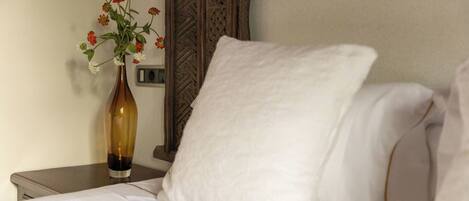 A neatly made bed with white linens, a white pillow, and a vase with flowers on a bedside table.