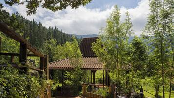 A wooden pathway leading to a rustic building with a tiled roof, surrounded by lush greenery and trees.