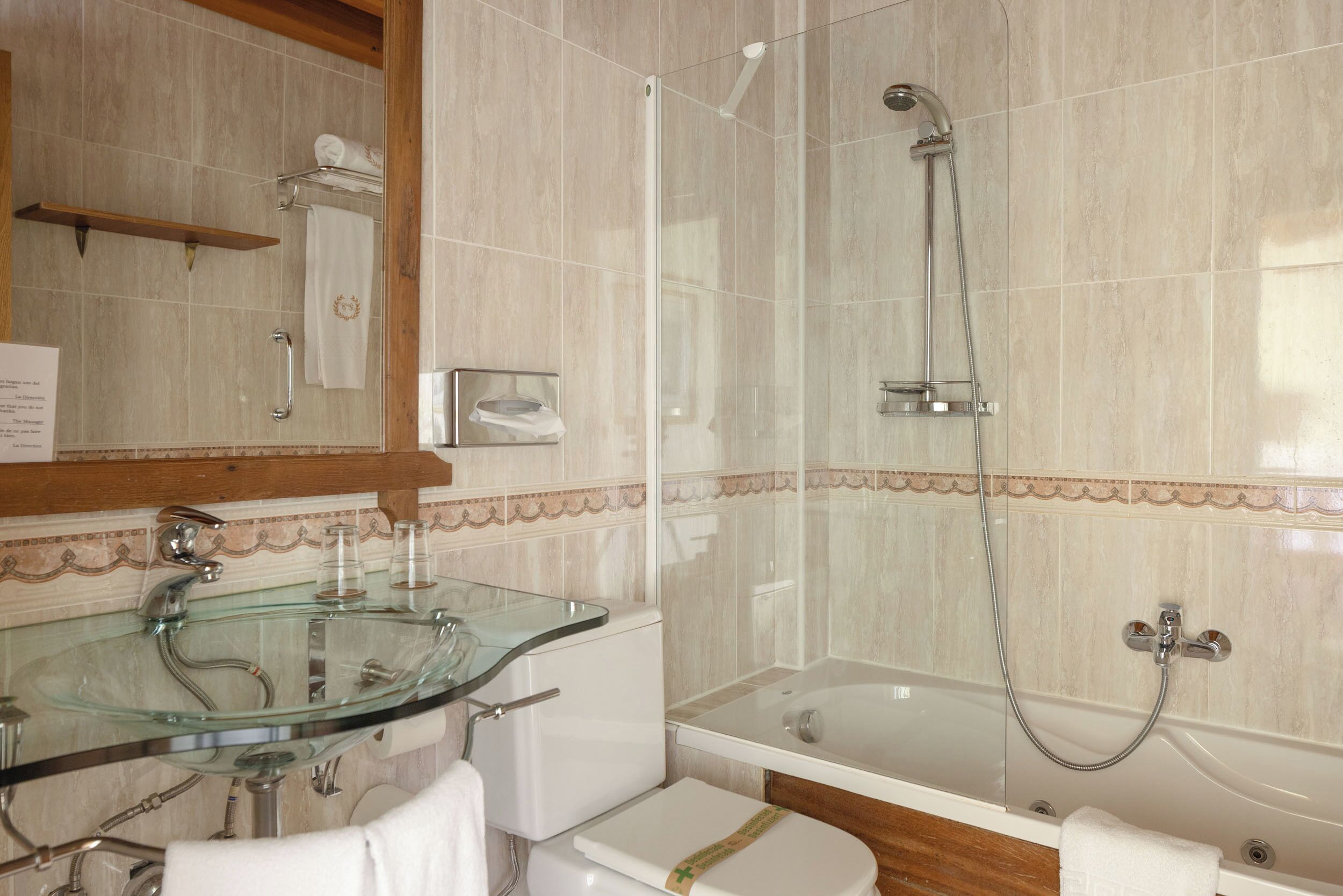 A bathroom with a glass sink, a toilet, a bathtub, and a shower.