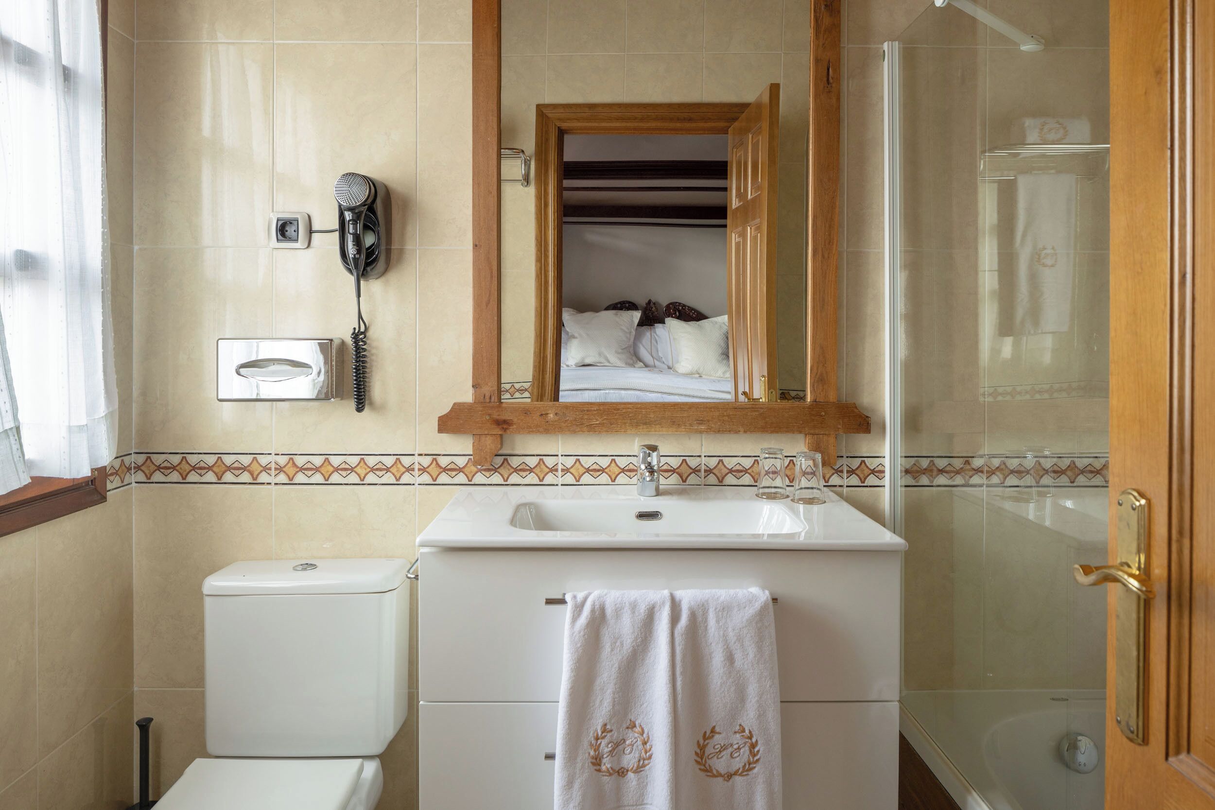 A bathroom with a toilet, sink, and shower. There is a towel hanging on the sink and a hairdryer mounted on the wall.