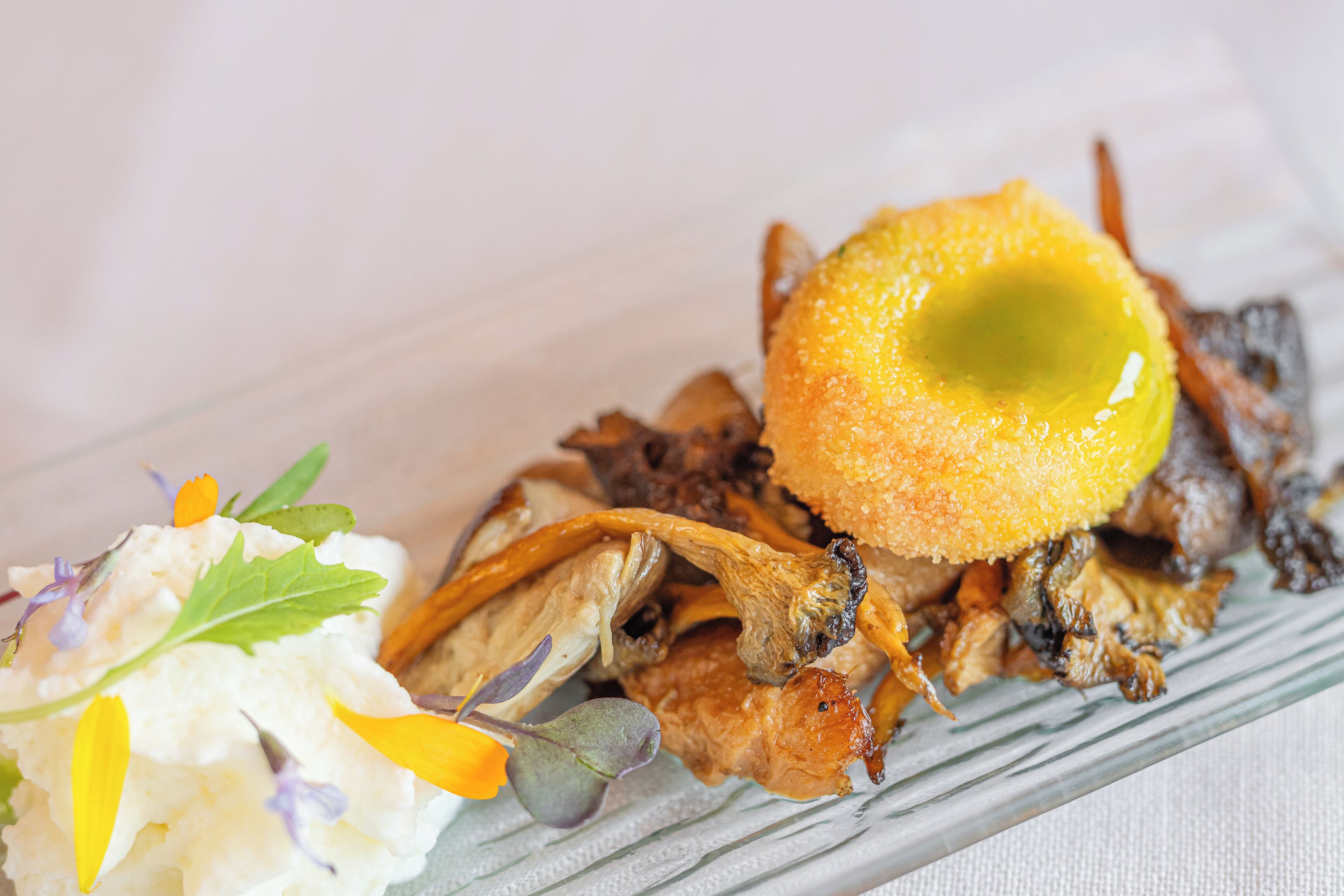 A plate with a variety of food items including a piece of meat, mushrooms, and a garnish of herbs and flowers.