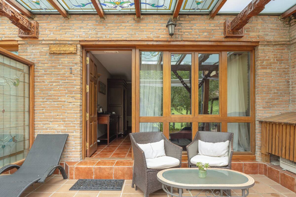 A sunlit patio with wicker furniture, a glass table, and a view of a brick building.
