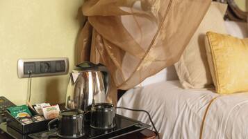 Een hotelkamer met een nachtkastje waarop een koffiezetapparaat, een dienblad met koffiekapsules en een kopje staan.