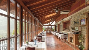 A spacious dining area with large windows, wooden beams, and a stone wall with a fireplace. - Etxegana Hotel & Spa (Zeanuri)