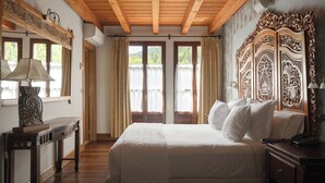 A hotel room with a wooden ceiling, a large bed with white linens, a wooden nightstand, a desk with a lamp, and a large ornate mirror. - Etxegana Hotel & Spa (Zeanuri)
