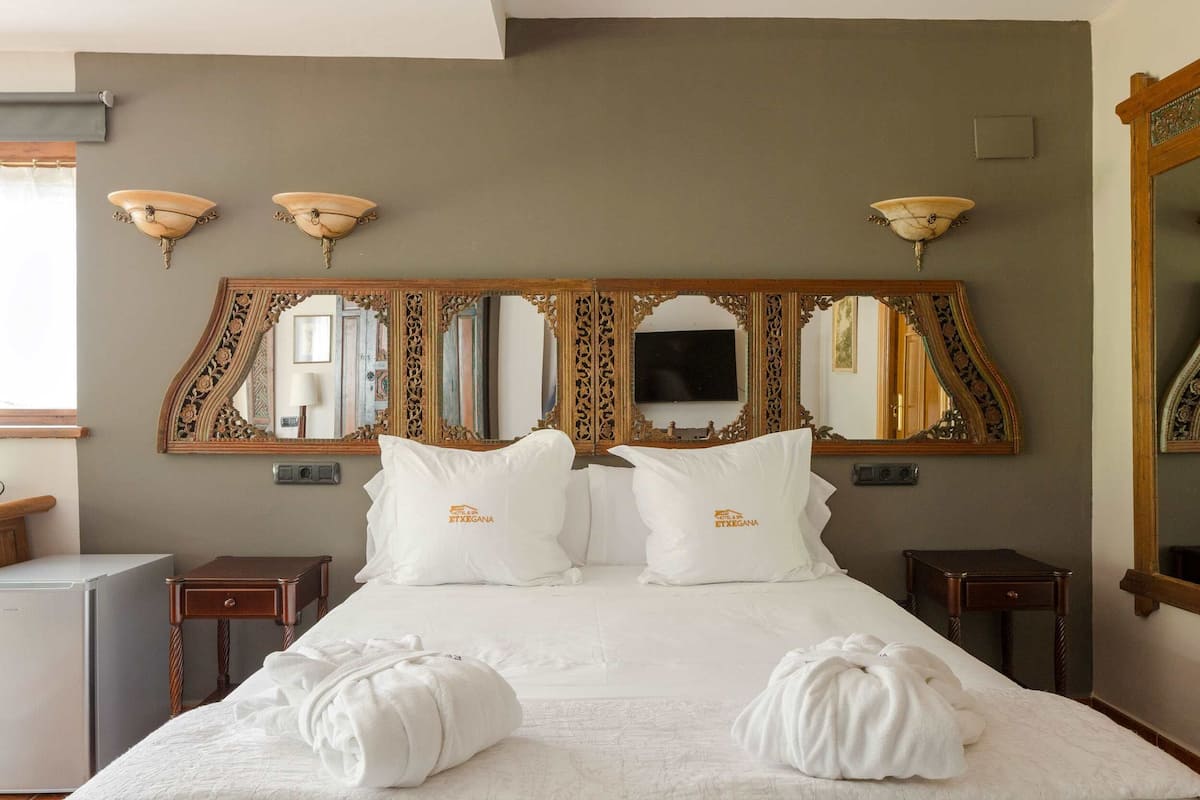 A hotel room with a large bed, two bedside tables, and a wall-mounted mirror with ornate designs.