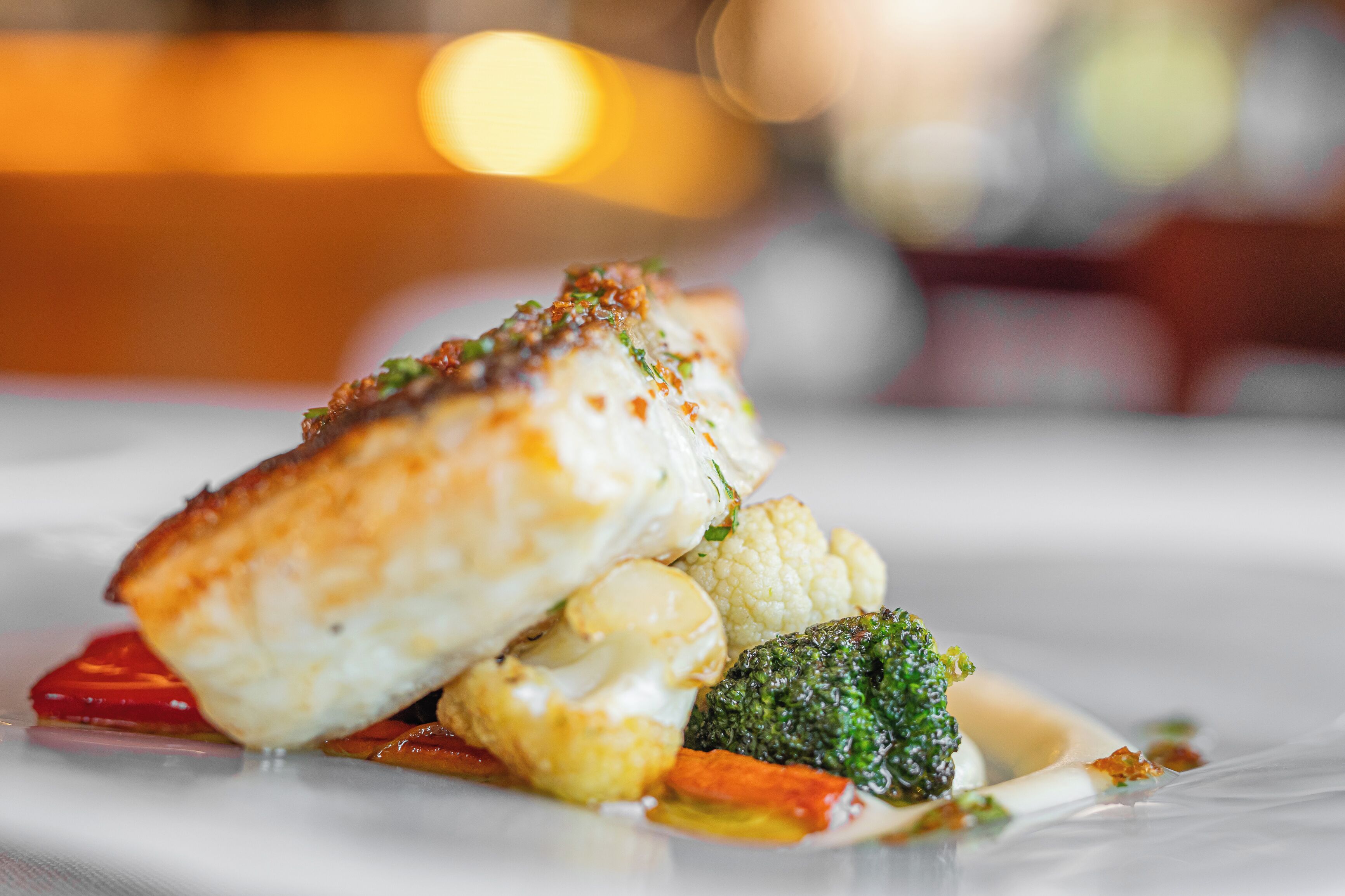 A plate of food with a piece of fish, cauliflower, broccoli, and sauce.