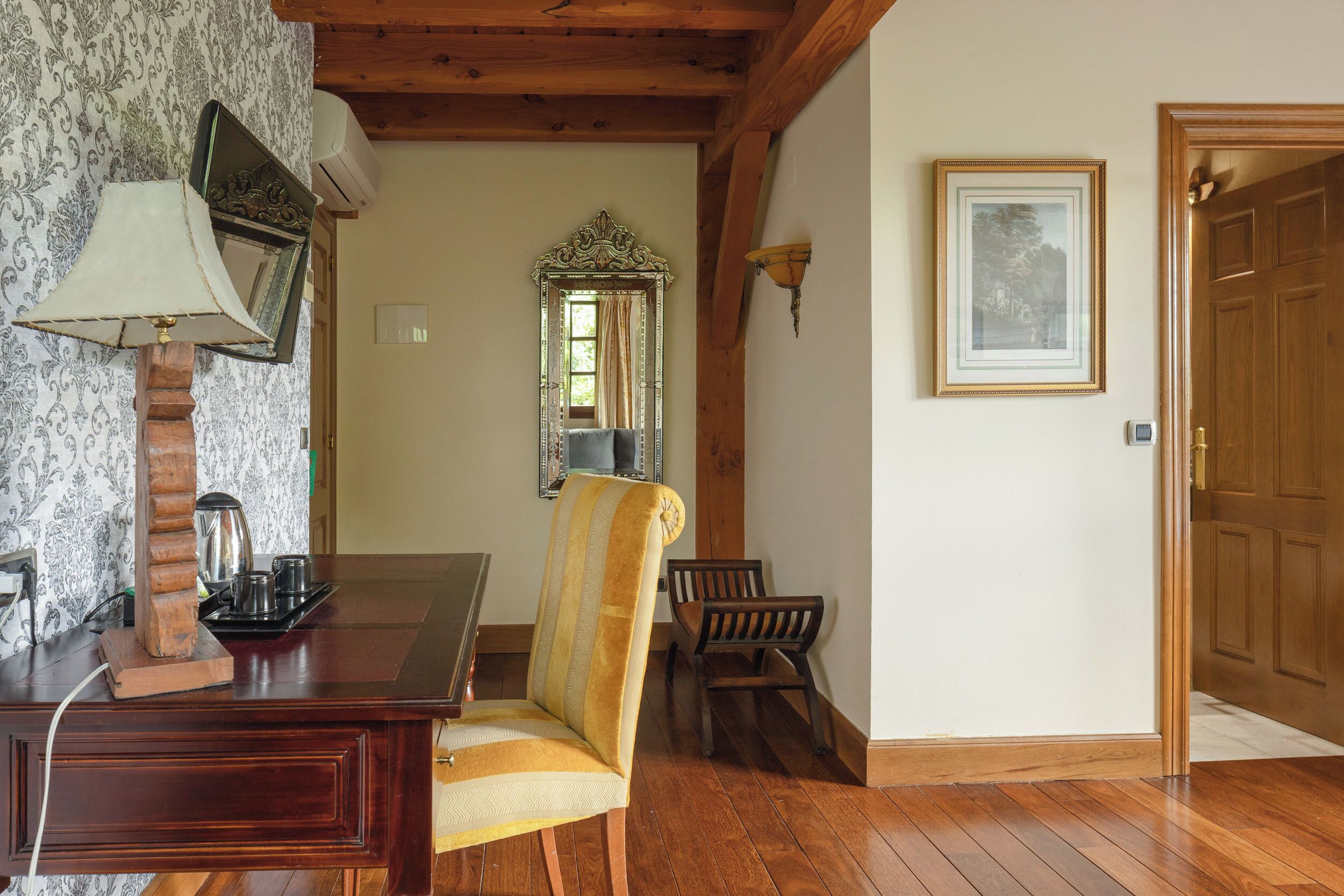 A wooden dining table with a lamp, a chair, a mirror, and a framed picture on the wall.