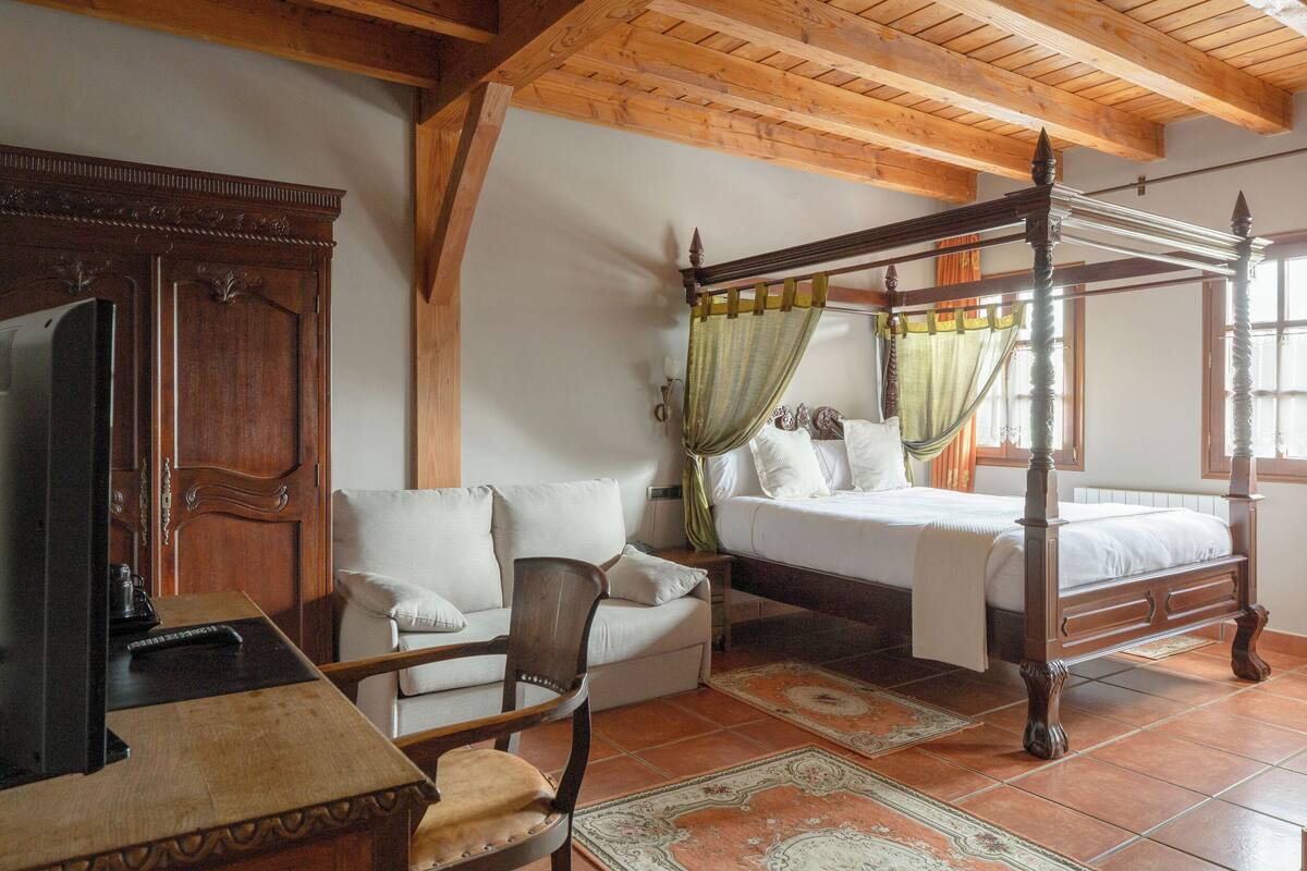 A traditional bedroom with a four-poster bed, a wooden wardrobe, a sofa, and a table.