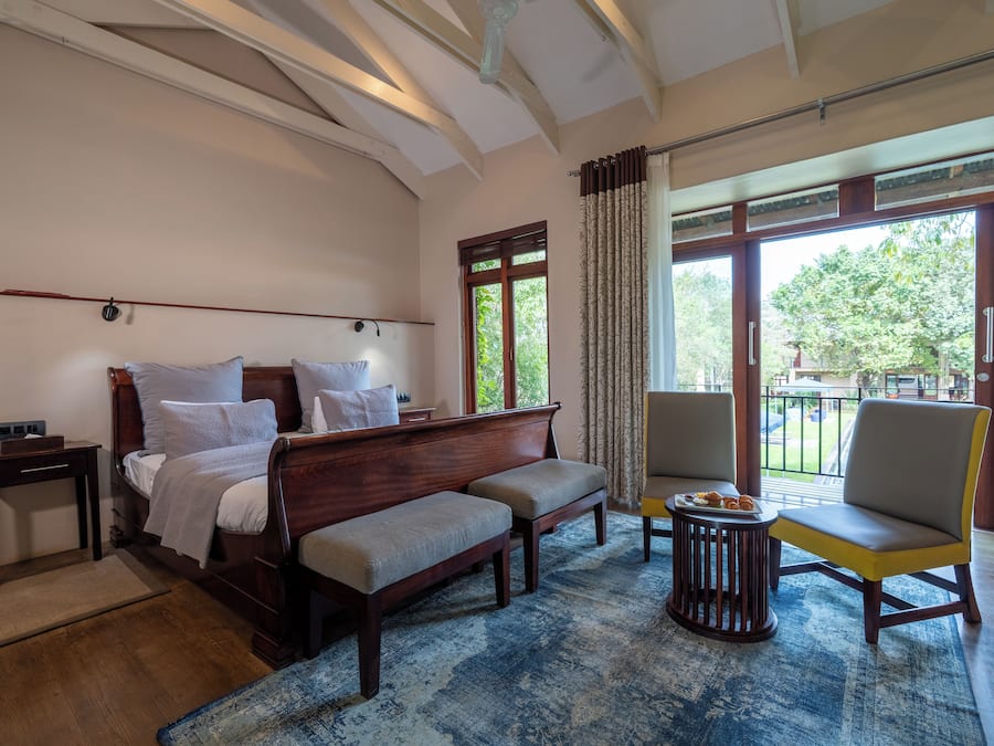 A hotel room with a bed, a sofa, a chair, a small table with pastries, and a view of the outdoors.