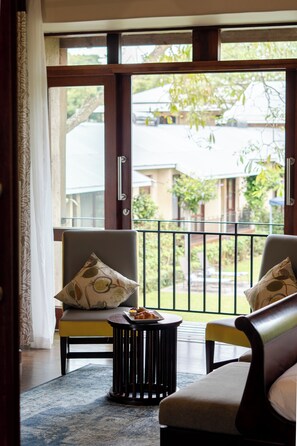 Une pièce comprenant un canapé, un fauteuil, une petite table avec des pâtisseries, et une vue sur l’extérieur à travers une porte vitrée.