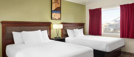 A hotel room with two beds, a nightstand with a lamp, a framed picture on the wall, and a window with red curtains.